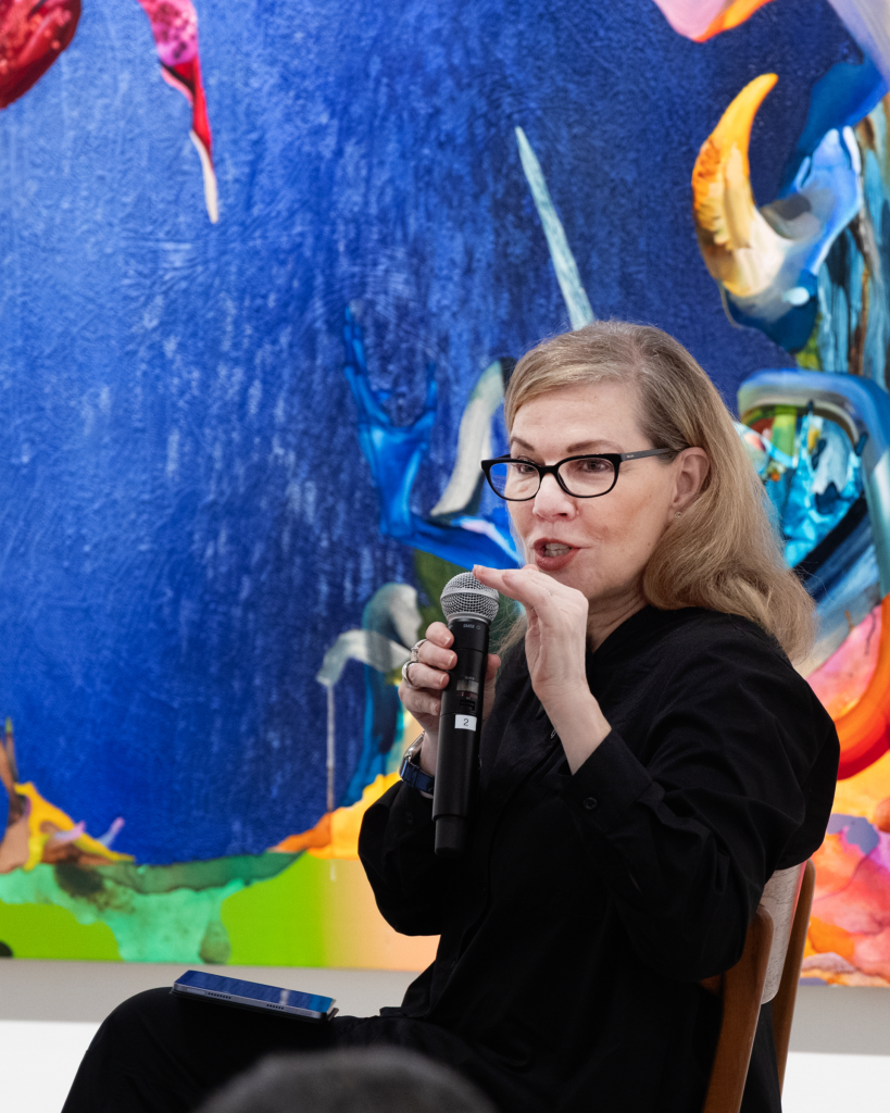 Debbie Millman holding a microphone in front of a painting