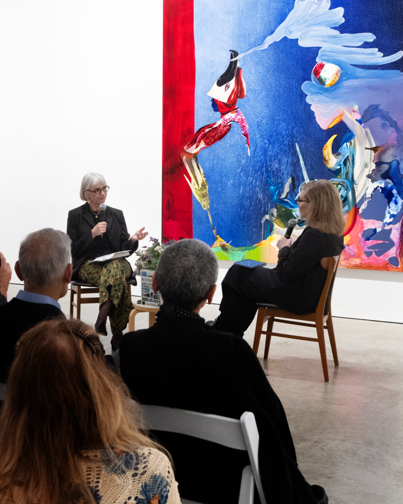Debbie Millman speaking with an audience in front of a large painting